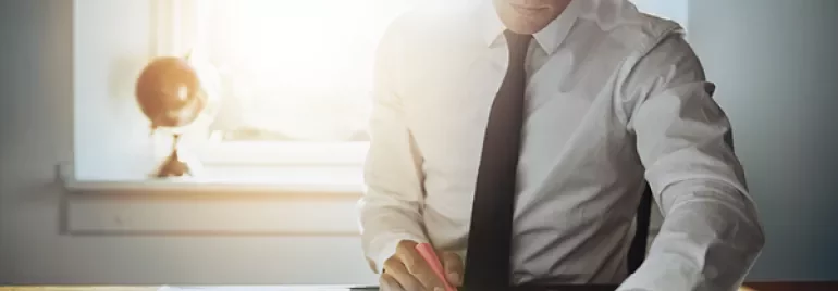Person working at a desk with documents and a calculator in sunlight.