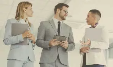Three people in business attire discussing in an office setting.