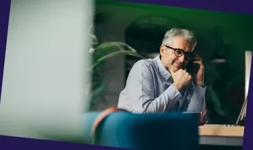Person talking on a phone while working at a desk with a laptop in an office setting.