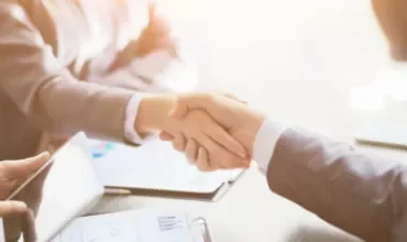 Two people shaking hands over a table with documents.