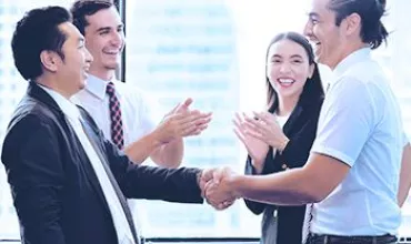 Group of people in business attire shaking hands and clapping in an office setting.