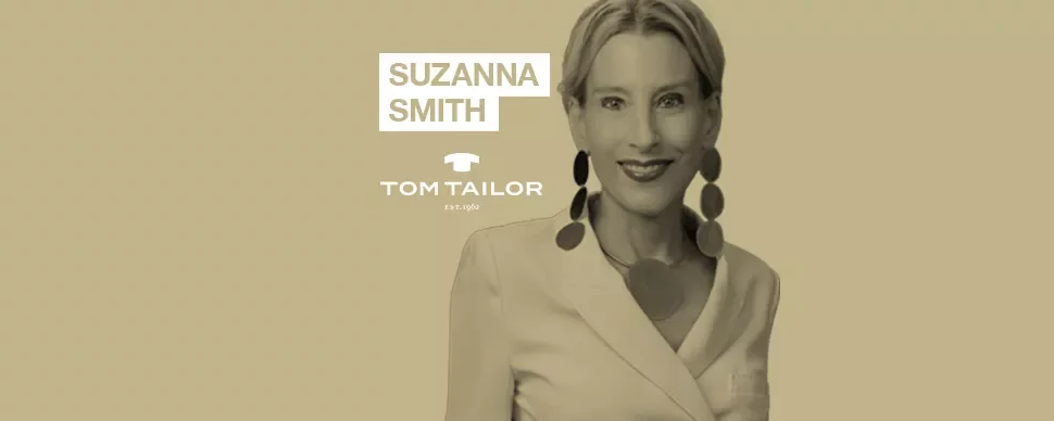 Person smiling, wearing a white blazer and large earrings, with text 'SUZANNA SMITH' and 'TOM TAILOR'.