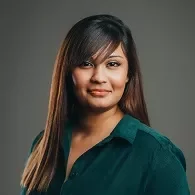 Person smiling wearing a green blouse against a gray background.