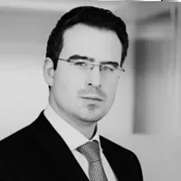 Person in a suit and tie wearing glasses, looking at the camera.