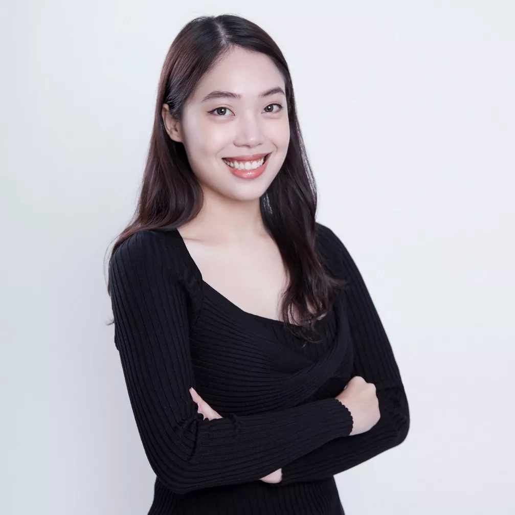 Person smiling with arms crossed, wearing a black top against a light background.