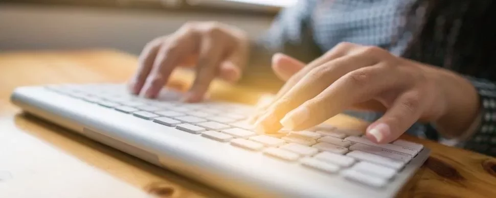 Close-up of hands typing on a white keyboard.