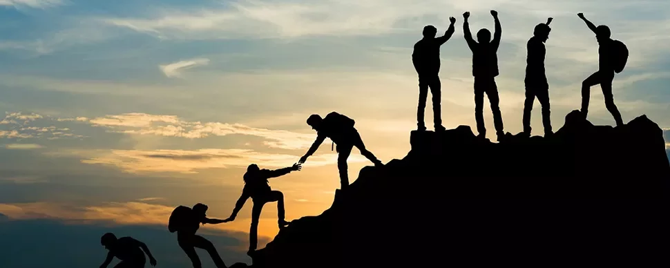 Silhouette of climbers helping each other on a mountain at sunset.