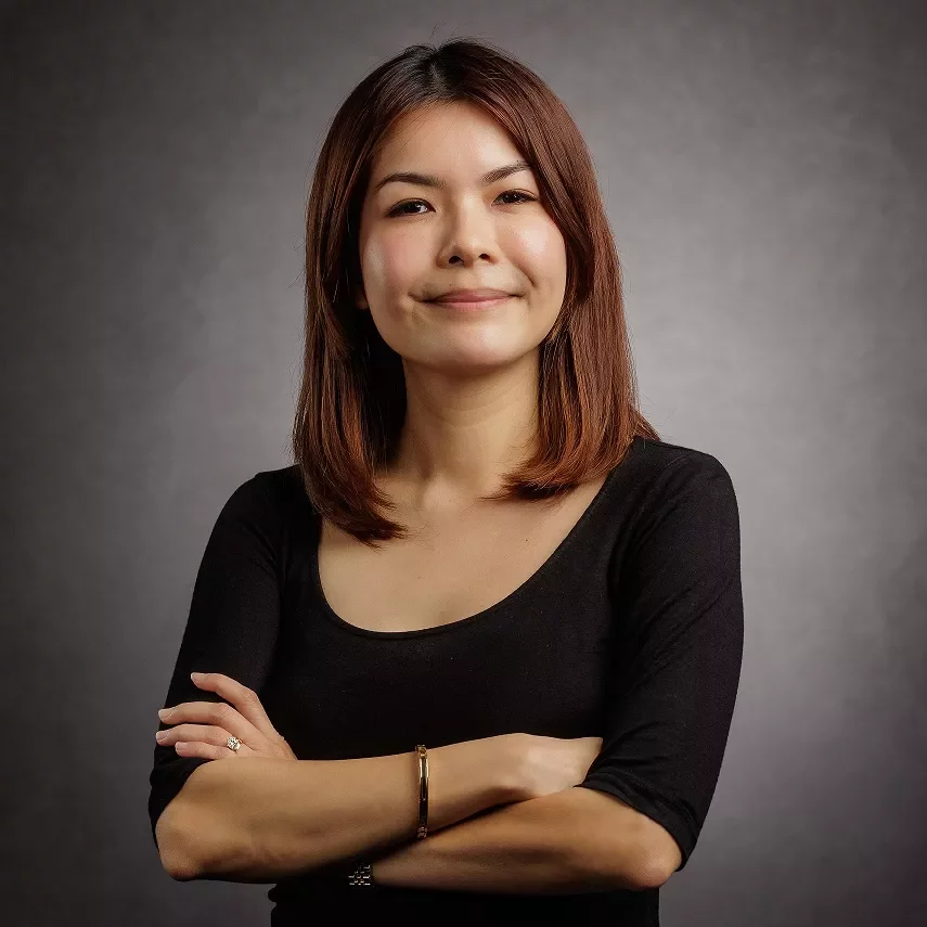 Person smiling with arms crossed, wearing a black shirt, against a gray background.