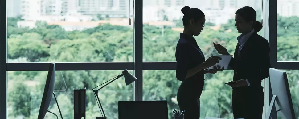 Two individuals discussing in an office with a window view of the city.
