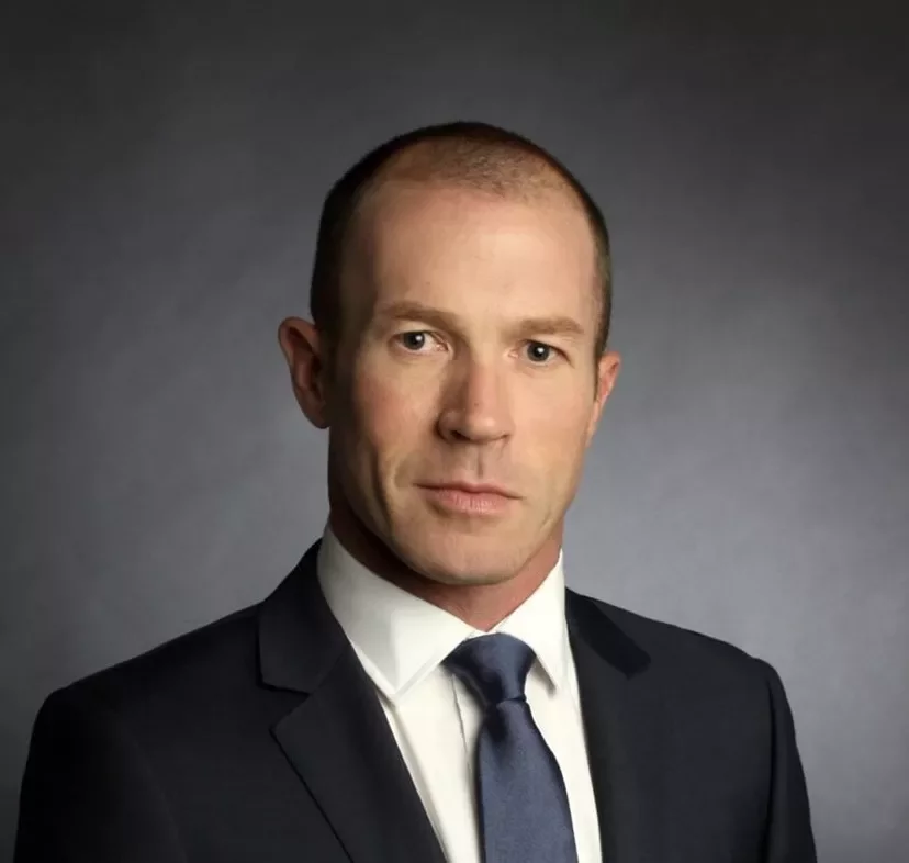 Person in a formal suit against a dark background.