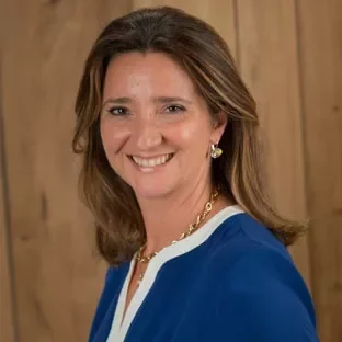 Person with medium-length hair, smiling, wearing a blue top against a wooden background.