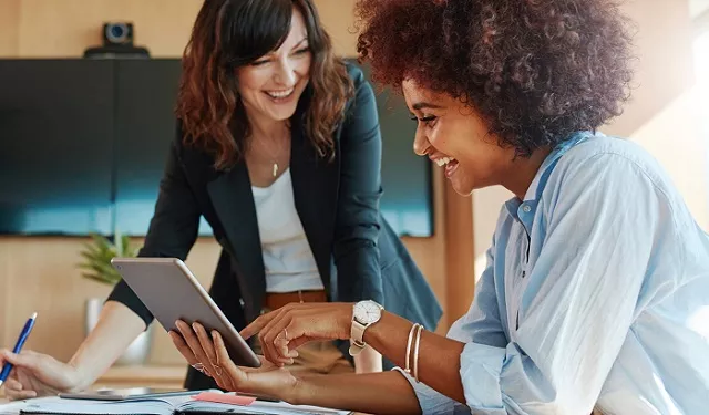 Two people smiling while looking at a tablet in an office setting.