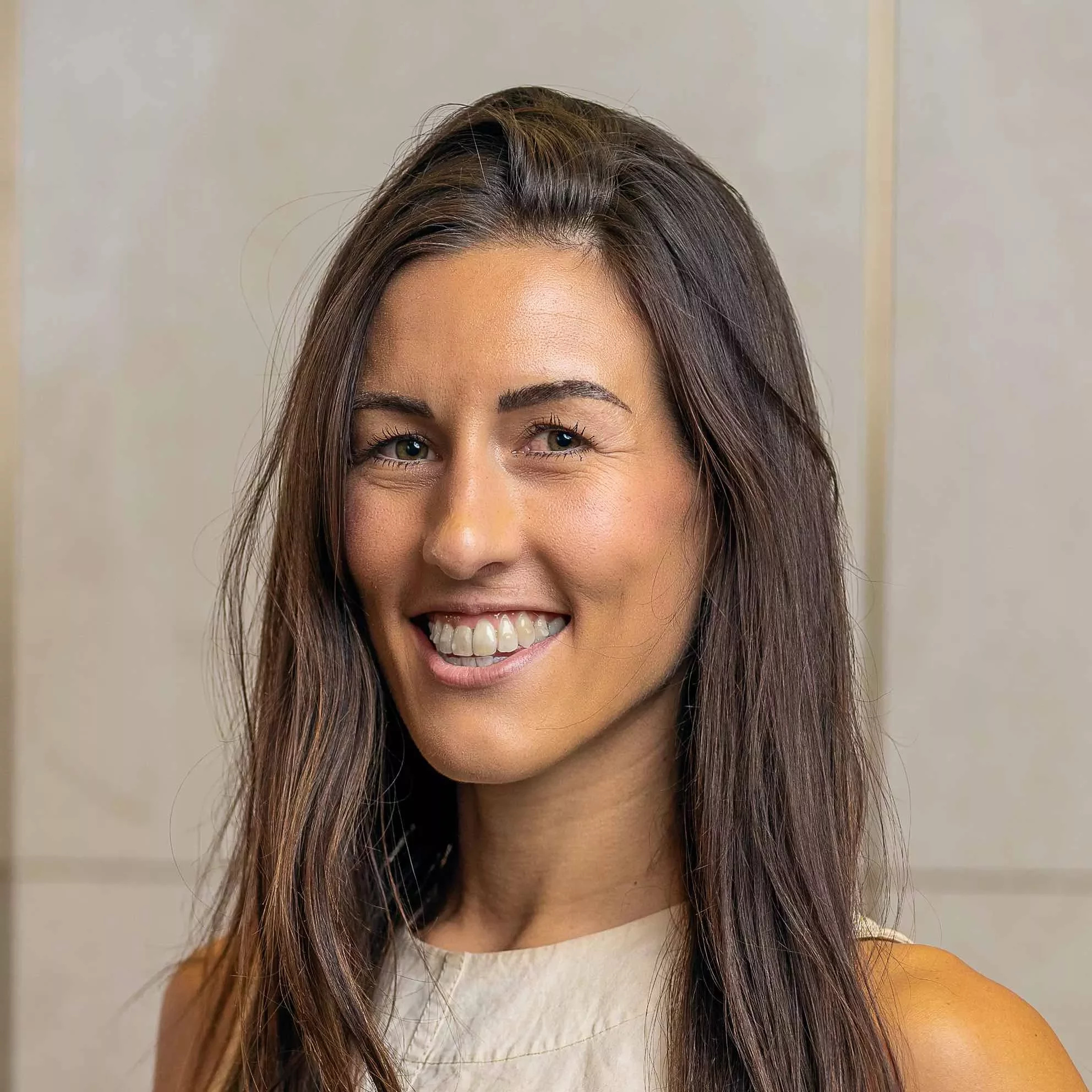 Person with long brown hair smiling warmly in a neutral background.