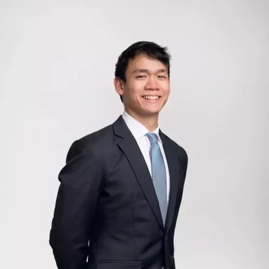 Person in a dark suit and blue tie smiling at the camera.