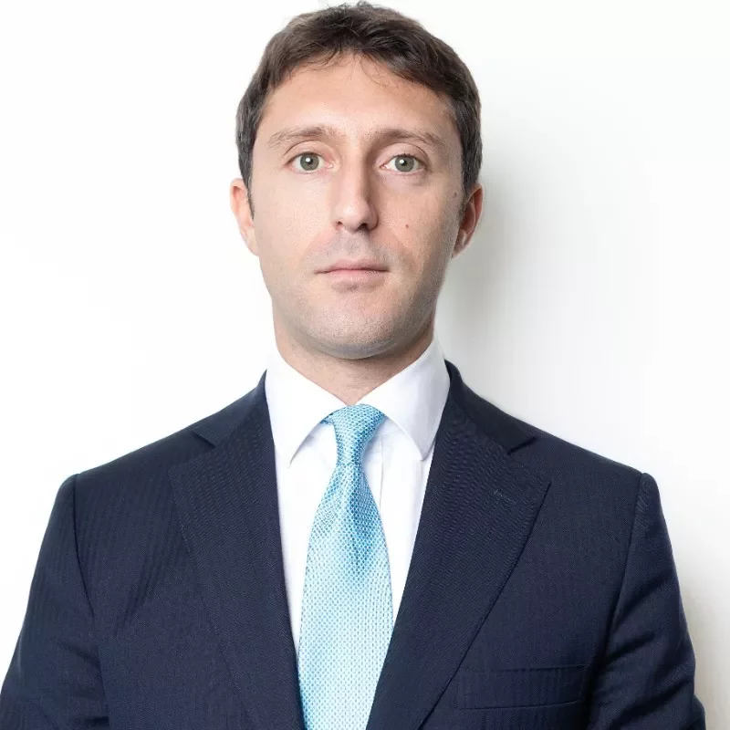 Person in a suit with a blue tie against a white background.