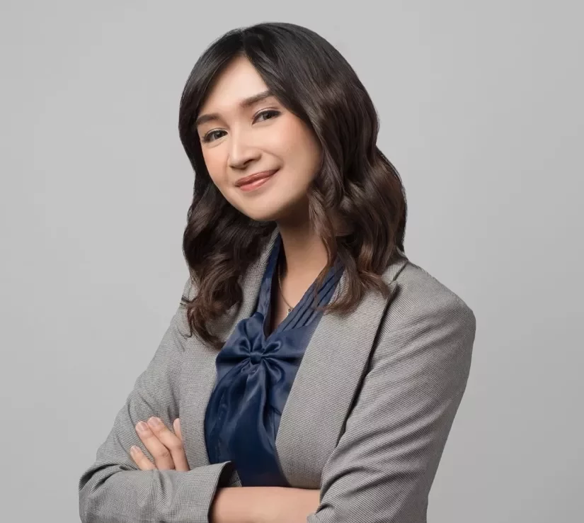 Person smiling with crossed arms, wearing a gray blazer and blue blouse.