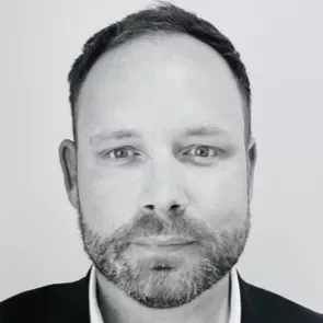 Black and white portrait of a person with short hair, wearing a suit jacket, looking directly at the camera.