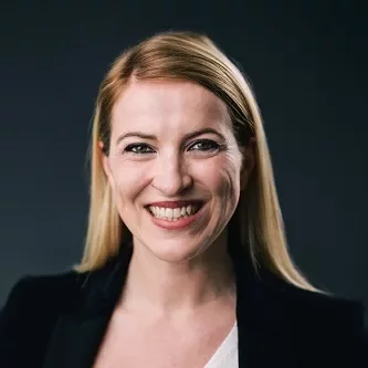 Person smiling in professional attire against a dark background.