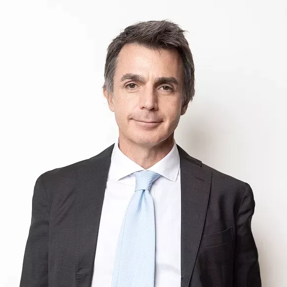 Person in suit with light blue tie against a white background.