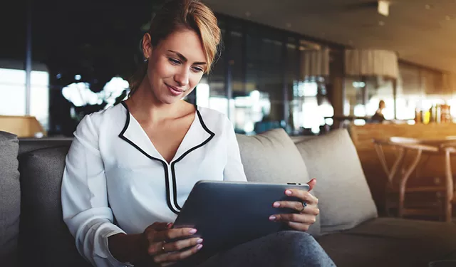 Person smiling while using a tablet on a sofa in a modern room.