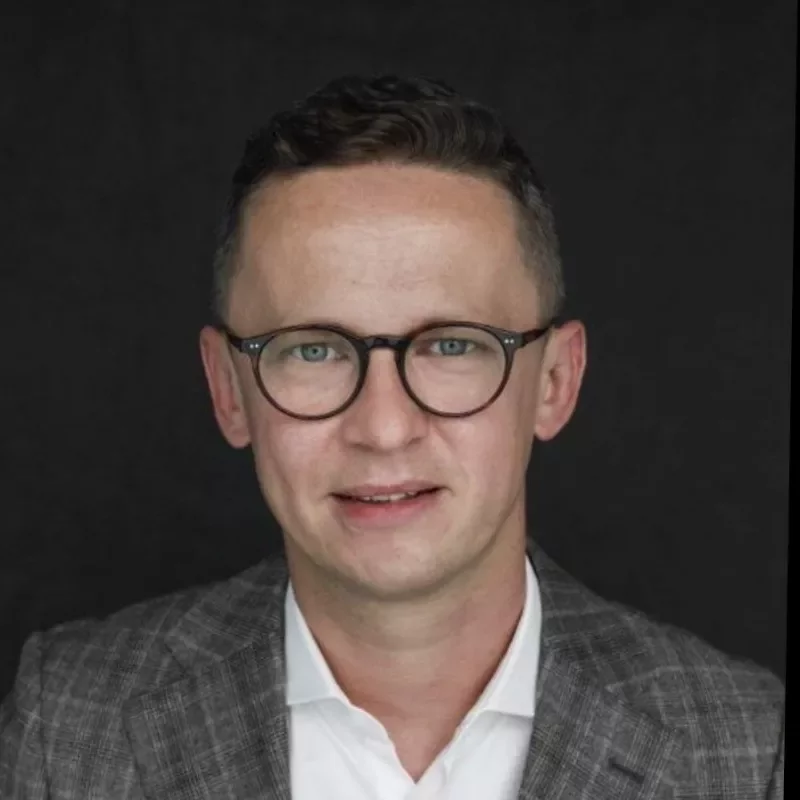 Individual wearing glasses and a suit, smiling at the camera.