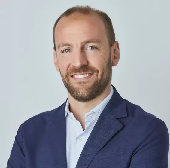 Person in a blue blazer, smiling and standing against a light background.