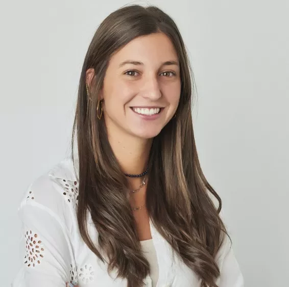 Smiling person with long hair wearing a white blouse.
