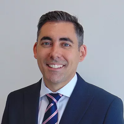 A person in a suit smiling against a plain background.