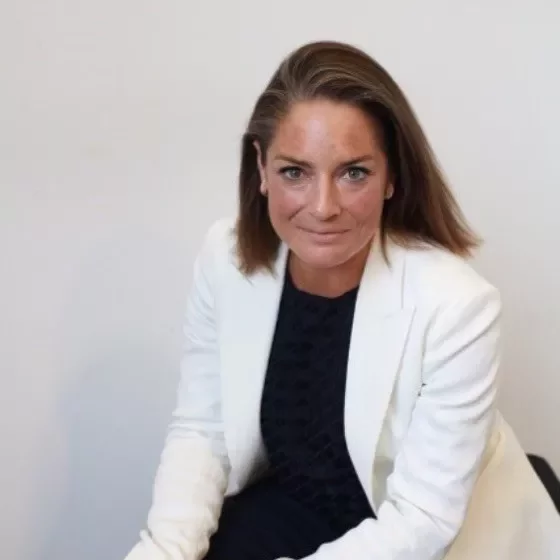 A person in a white jacket sitting and looking at the camera against a plain background.