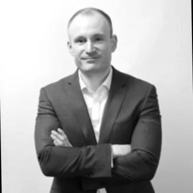 Person in a suit standing with arms crossed against a light background.