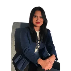 Person sitting on a chair, smiling, wearing a blue blazer and white top.