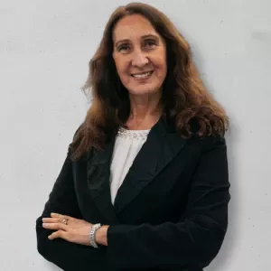 Person smiling, wearing a dark blazer, arms crossed in front of light gray background.