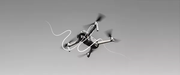 A quadcopter drone in mid-flight with motion blur on its propellers, set against a gray background.