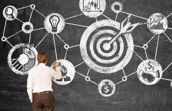 Person drawing a flowchart on a blackboard with target symbols and graphs.