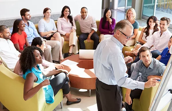 A group of people in a relaxed meeting setting with a speaker at the front.