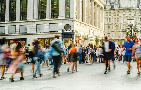 A bustling city street with people walking past shops.