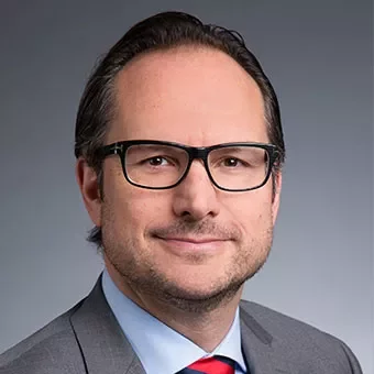 Person in glasses wearing a suit, smiling.