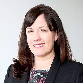 Person smiling, wearing a dark blazer, neutral background.