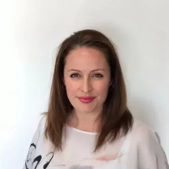Person with medium-length hair, wearing a light-colored top, smiles against a white background.