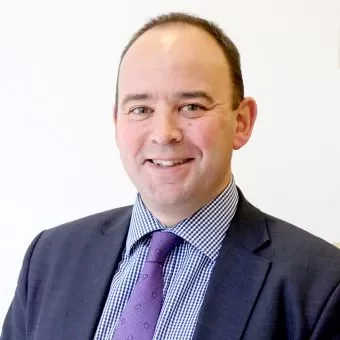Person smiling in a suit with a white background.
