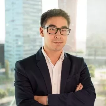 Person in a suit with glasses stands confidently in front of a window with city buildings in the background.