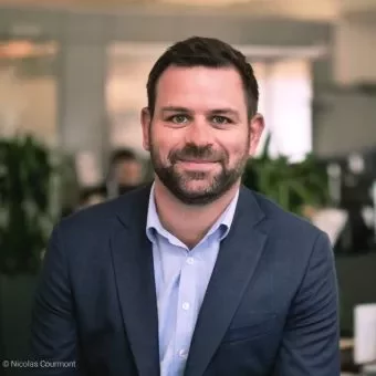 Person in a blue suit smiling in an office setting.