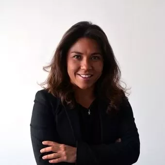 A person with long hair smiling, wearing a black suit against a white background.