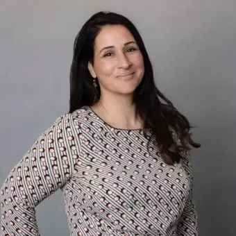 Person smiling in front of a gray background, wearing a patterned top.