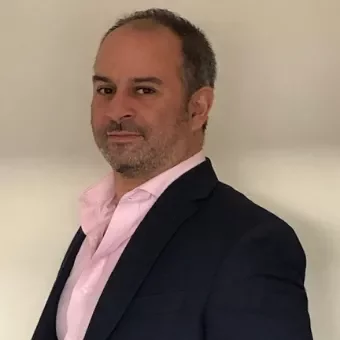 Person in a blazer and pink shirt, standing against a plain background.